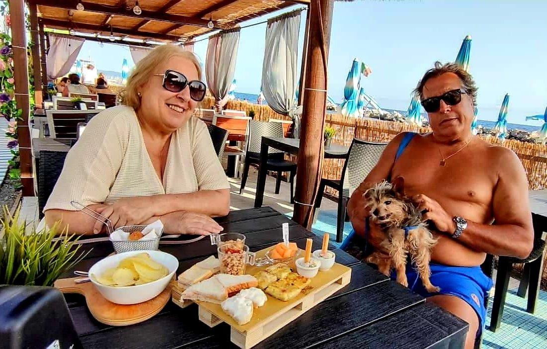 A couple of women sitting at a table with food and a dogDescription automatically generated with medium confidence