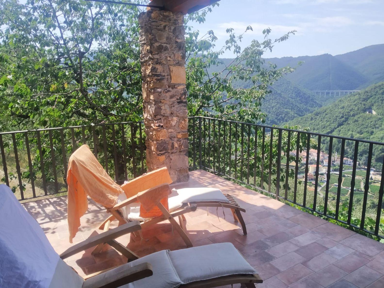 A deck with a table and chairs on it with trees and mountains in the backgroundDescription automatically generated with low confidence