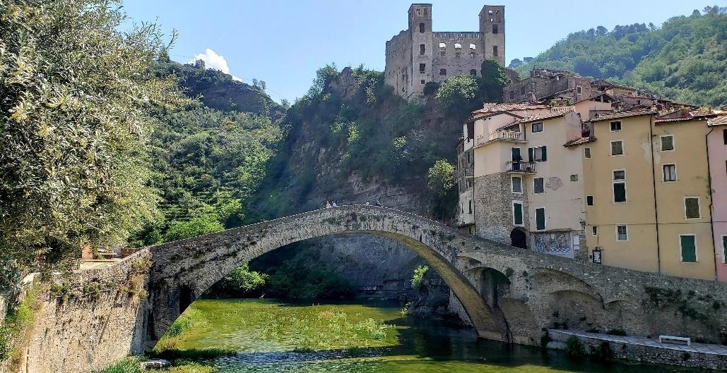 A stone bridge over a river with a castle in the backgroundDescription automatically generated