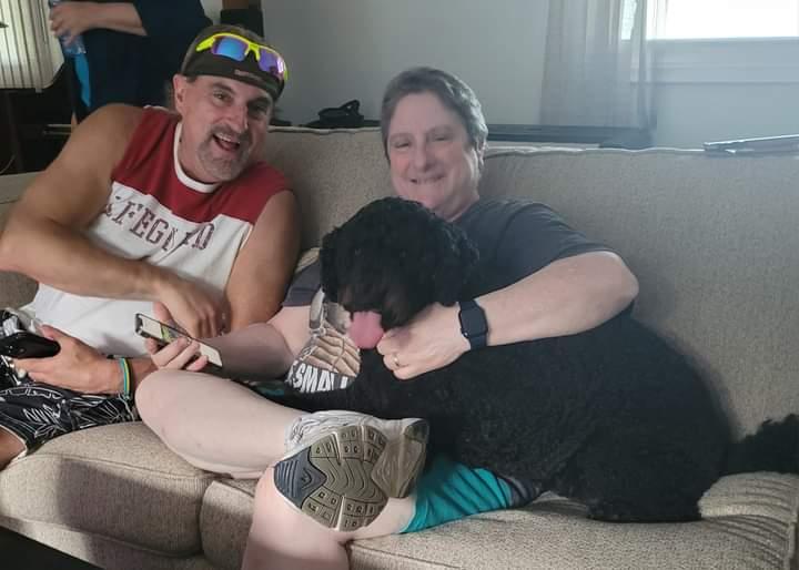 A person and person sitting on a couch with a dogDescription automatically generated
